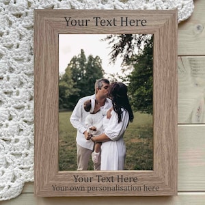 May include: A wooden picture frame with a photo of a family of three in a park. The frame has a personalized inscription that reads "Your Text Here Your own personalisation here".
