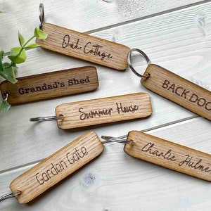 May include: Six wooden keychains with engraved text. The keychains are labeled "Oak Cottage", "Grandad's Shed", "Summer House", "Back Door", "Garden Gate", and "Charlie Hulme".