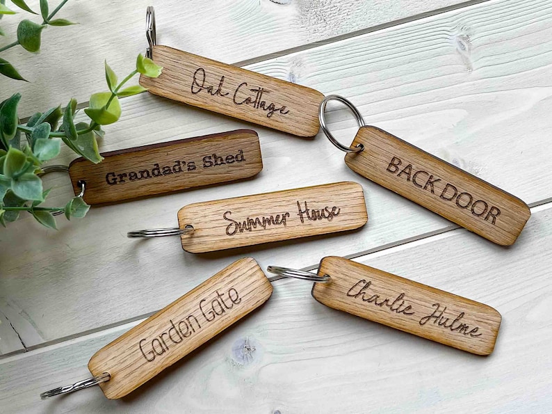 May include: Six wooden keychains with engraved text. The keychains are labeled "Oak Cottage", "Grandad's Shed", "Summer House", "Back Door", "Garden Gate", and "Charlie Hulme".