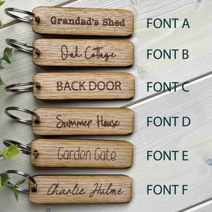 May include: Six wooden keychains with different fonts and text. The text on the keychains reads: "Grandad's Shed", "Oak Cottage", "BACK DOOR", "Summer House", "Garden Gate", and "Charlie Hulme".