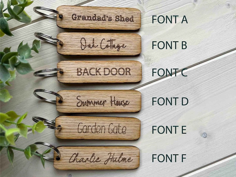 May include: Six wooden keychains with different fonts and text. The text on the keychains reads: "Grandad's Shed", "Oak Cottage", "BACK DOOR", "Summer House", "Garden Gate", and "Charlie Hulme".