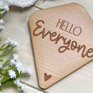 May include: A diamond-shaped wooden sign with rounded edges. The sign is light brown and has the text "HELLO everyone" engraved on it. There is a small heart shape at the bottom of the sign.