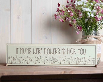 May include: A light green wooden sign with the text "If mums were flowers I'd pick you" in brown lettering. The sign is decorated with a row of small, stylized flowers along the bottom.