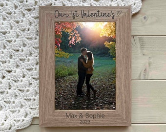 May include: A wooden photo frame with a picture of a couple kissing in a forest. The frame has the text "Our 1st Valentine's" at the top and "Max & Sophie 2023" at the bottom.