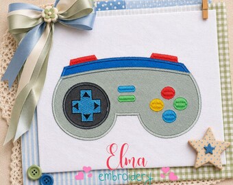 Peut inclure: Un motif de manette de jeu grise, bleue et rouge. La manette comporte un pavé directionnel, des boutons et une bordure bleue. Le motif est sur un fond blanc avec un ruban bleu et vert et un ornement en forme d'étoile. Le texte "Elma embroidery" est visible.
