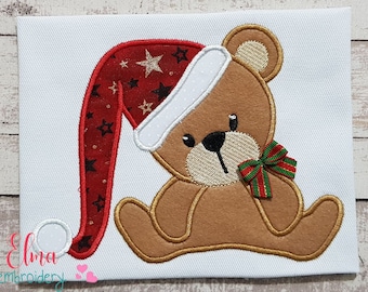 May include: Embroidered design of a brown teddy bear wearing a red and white Santa hat with gold stars and a green and red bow.