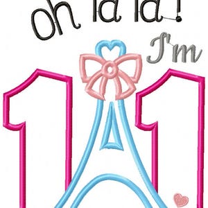 K&ouml;nnte beinhalten: Ein Stickdesign mit dem Text oh la la! I'm in Schwarz und Grau, sowie der Zahl 11 in leuchtendem Pink. Eine hellblaue Eiffelturm-Grafik befindet sich zwischen den Zahlen, gekr&ouml;nt von einer zartrosa Schleife und einem kleinen rosa Herz am Fu&szlig;.