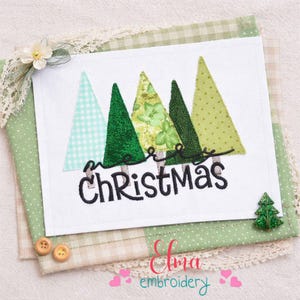 Puede incluir: Un cuadrado blanco con árboles de Navidad verdes bordados y las palabras "Merry Christmas" en escritura negra. El diseño está sobre un fondo de patchwork de telas verdes y beige, con un pequeño adorno de árbol verde.