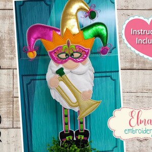 K&ouml;nnte beinhalten: Ein Mardi Gras-Zwerg mit einer goldenen, orangen, pinken und gr&uuml;nen Narrenkappe, einer pinken und goldenen Maske und einer goldenen Trompete. Der Zwerg steht auf einer gr&uuml;nen Pflanze. Der Text "Instructions Included" befindet sich in einem pinken Herz. Der Text "Elma embroidery" befindet sich in einem cremefarbenen Oval mit pinkem Rand.