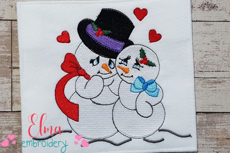 Pu&ograve; includere: Disegno ricamato di due pupazzi di neve che si abbracciano, con fiocchi rossi e blu, con cuori e dettagli di agrifoglio. Il testo "Elma embroidery" &egrave; in basso.