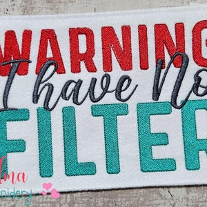 May include: White rectangular embroidered patch with the words "WARNING I have No FILTER" in red, gray, and teal. The patch is surrounded by decorative flowers in shades of teal and red.