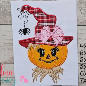 May include: Embroidered design of a pumpkin wearing a red and black plaid witch hat with a pink bow and a spider hanging from the hat. The pumpkin has a smiling face with eyelashes and a straw-like beard. The design is available in sizes 4x4, 5x4, 5x7, 5x8, 6x10, and 7x12 inches.