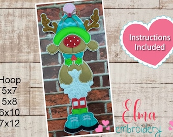 May include: A whimsical Christmas reindeer design with a green and blue hat, red nose, and brown antlers. The design includes a decorative collar and legs with green shoes. The text "Instructions Included" is visible.