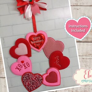 May include: A Valentine's Day wreath made of felt hearts in red and pink with embroidered sayings like "Happy Valentine's Day", "XOXO", and "Be Mine". The wreath is decorated with a red bow and a small strawberry. Instructions are included. The wreath can be made with a 5x7, 6x10, or 7x12 hoop.