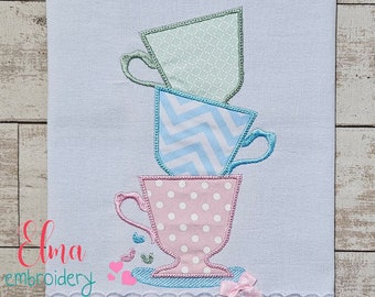 May include: Three stacked teacups with different patterns. The top cup is green with a diamond pattern, the middle cup is blue with a chevron pattern, and the bottom cup is pink with white polka dots. The cups are on a white background.