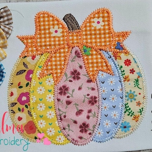 May include: A patchwork pumpkin design with a gingham bow and floral accents. The pumpkin is made of various patterned fabrics in yellow, pink, blue, and orange. Three decorative bows with wooden buttons are to the left. Sizes available: 4x4, 5x5, 6x6, 7x7.