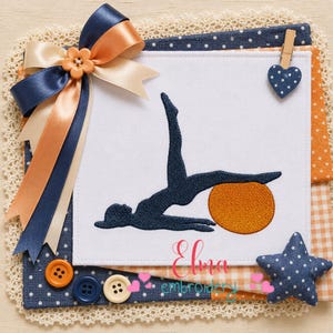 May include: A white fabric square featuring a dark blue embroidered silhouette of a person doing a bridge pose with an orange exercise ball. The square is decorated with a navy, peach, and cream ribbon bow, a blue heart clip, and a blue star.
