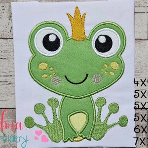 May include: Embroidered design of a green frog wearing a gold crown. The frog has large, white eyes with black pupils and a small, happy smile. The design is available in various sizes, including 4x4, 5x4, 5x7, 5x8, 6x10, and 7x12 inches.