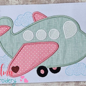 以下が含まれることがあります： 緑の飛行機の刺繍アップリケデザイン。ピンクの翼と白いディテール。飛行機には丸い窓が3つと、翼に小さなハートがあります。デザインは青い雲で囲まれています。サイズは4x4、5x4、5x7、5x8、6x10、7x12インチです。