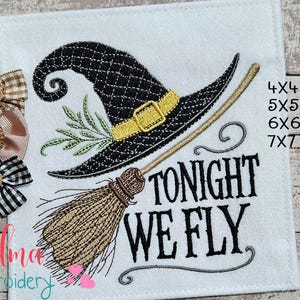 Puede incluir: Tela blanca con un sombrero de bruja negro, una escoba y el texto "TONIGHT WE FLY". El sombrero tiene una hebilla dorada y está decorado con hojas verdes. Tres lazos decorativos a la izquierda.