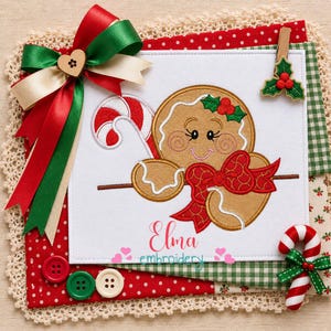 Puede incluir: Un cuadrado de tela blanca con el bordado de una figura de pan de jengibre que sostiene un bastón de caramelo rojo y blanco, decorado con un lazo rojo. El texto Elma embroidery está bordado debajo. Un gran lazo de cinta rojo, verde y crema.