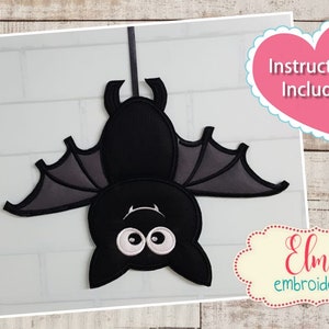 May include: A black bat with white eyes hanging from a string. The bat is designed for in-the-hoop embroidery and is available in 5x7, 6x10, and 7x12 hoop sizes. Instructions are included. Elma embroidery.