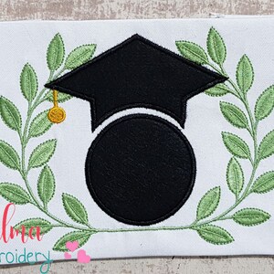 May include: Black graduation cap with a gold tassel, surrounded by a green laurel wreath. The cap is over a black circle with space for personalization.
