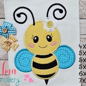Può includere: Disegno di ape ricamato con ali blu, corpo giallo e strisce nere. L'ape ha un fiore bianco sulla testa e un viso sorridente. Il design è disponibile nelle dimensioni 4x4, 5x4, 5x7, 5x8, 6x10 e 7x12 pollici.