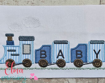 Peut inclure: Train brodé bleu et blanc avec le mot "BABY" écrit sur les wagons. Le train a une cheminée et des roues brunes.