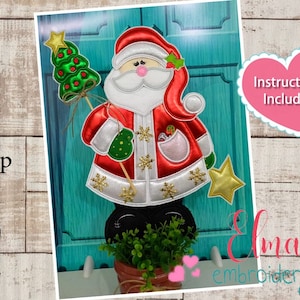 May include: Embroidered design of Santa Claus holding a Christmas tree, with a gold star on top, against a turquoise background. The design is available in 5x7, 6x10, and 7x12 hoop sizes. Instructions are included.