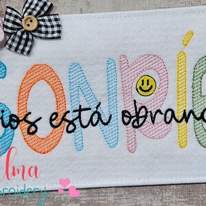 May include: Embroidered design with the text "SONRIE Dios esta obrando" in rainbow colors with a smiley face. The design is available in sizes 4x4, 5x4, 5x7, 5x8, 6x10, and 7x12 inches.