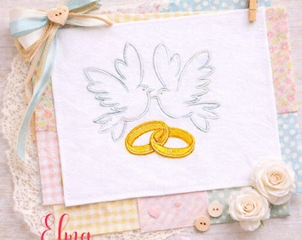 May include: A white embroidered square features two doves and two gold wedding rings. The design is set against a backdrop of pastel fabrics, lace, and decorative elements, including a bow and wooden buttons. The text "Elma embroidery" is visible.