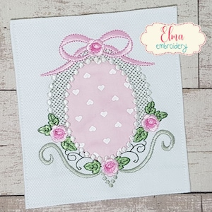 Könnte beinhalten: Stickerei eines rosa Ostereis mit weißem Tupfenmuster, umgeben von einem Blumengirlanden mit grünen Blättern und rosa Rosen. Eine rosa Schleife mit einem weißen Perlenmittelpunkt sitzt auf dem Ei. Das Design ist auf einem weißen Stoffhintergrund. Der Text "Elma embroidery" befindet sich in der oberen rechten Ecke.