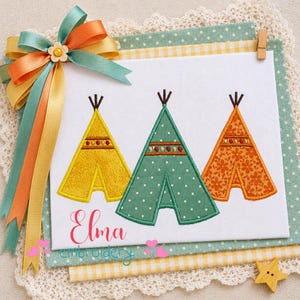 May include: Embroidered artwork featuring three colorful teepee designs in yellow, green, and orange. The artwork includes the name "Elma" in cursive script and the word "embroidery". A decorative ribbon and a wooden star accent the piece.