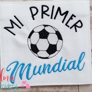 Könnte beinhalten: Weißer Filz-Patch mit schwarzer Stickerei, auf dem "Mi Primer Mundial" steht, mit einem schwarz-weißen Fußball in der Mitte.