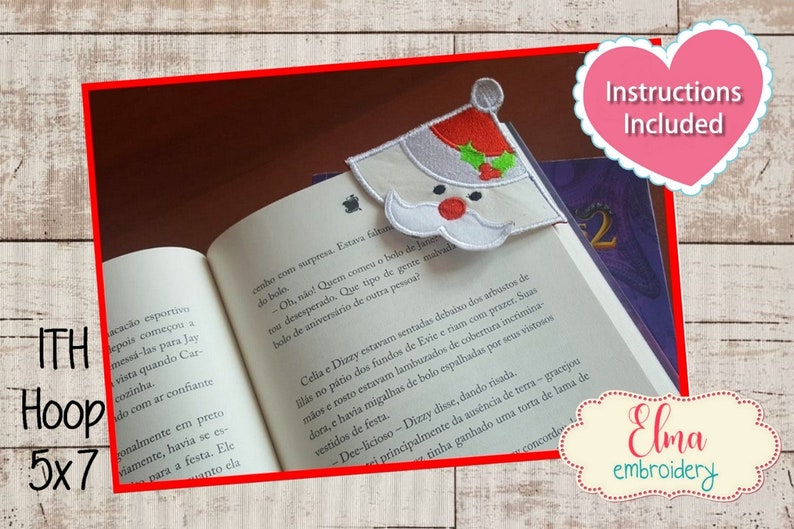 K&ouml;nnte beinhalten: Ein wei&szlig;-roter Weihnachtsmann-Lesezeichen mit einem gr&uuml;nen Stechpalmenzweig. Das Lesezeichen liegt auf einem Buch mit dem Text "Instructions Included" in einem rosa Herz. Das Lesezeichen ist f&uuml;r einen 5x7-Hoop.