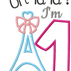 K&ouml;nnte beinhalten: Ein Stickmuster mit dem Text "oh la la ! I'm" in Schwarz und Grau. Unter dem Text befindet sich der Umriss eines hellblauen Eiffelturms mit einer rosa Schleife an der Spitze und eine gro&szlig;e rosa Zahl "1" mit einem kleinen rosa Herz.