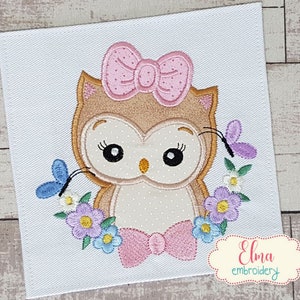 May include: Embroidered design of a brown owl with pink bow and flowers. The owl has large black eyes and a pink bow around its neck. The flowers are in shades of purple, blue, and white.