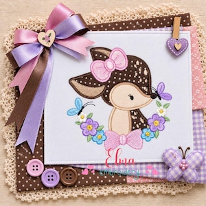 May include: A white fabric square featuring an embroidered brown fawn with a pink bow, surrounded by purple and blue flowers and butterflies. The square is decorated with a large lavender and brown ribbon bow, three buttons, and a purple butterfly.