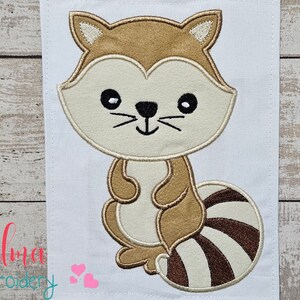 May include: Embroidered design of a brown and white raccoon with a striped tail. The raccoon is sitting upright with its paws in front of it.