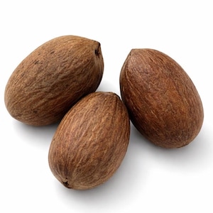 May include: Three whole brown nutmeg seeds with a textured, woody surface. Each seed has an oval shape with a slightly pointed end and a rough, fibrous exterior. The seeds are arranged in a cluster against a plain white background.
