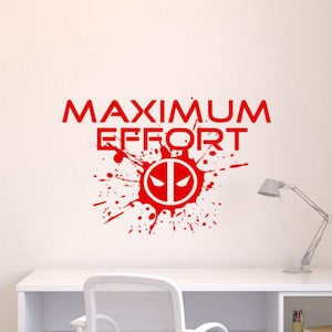 Peut inclure: Un autocollant mural rouge présentant le texte MAXIMUM EFFORT dans une police grasse sans empattement. Sous le texte se trouve une icône circulaire avec deux yeux angulaires, entourée d'un motif d'éclaboussures de peinture rouge.