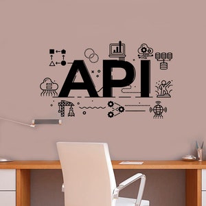 May include: A black and white illustration of the word "API" with various icons and symbols surrounding it, including a cloud, a computer, gears, and a globe. The illustration is on a light pink wall behind a white desk with a white chair.