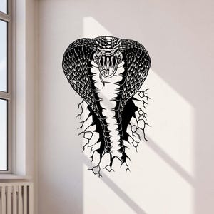 May include: A black and white graphic illustration of a cobra snake breaking through a cracked wall. The cobra is shown with its hood spread, fangs visible, and tongue protruding. The design features detailed patterns on the snake's scales.