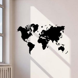 May include: A black world map decal is affixed to a white wall, showcasing the continents and countries. The decal is a solid black color, with a detailed outline of the world's landmasses. The wall is illuminated by natural light from a nearby window.