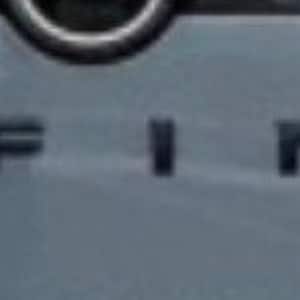 Puede incluir: Primer plano de un panel gris de vehículo con la palabra "PATHFINDER" en negro en el centro. Las letras son en negrita y espaciadas uniformemente. El panel tiene una ligera curva y un acabado brillante.