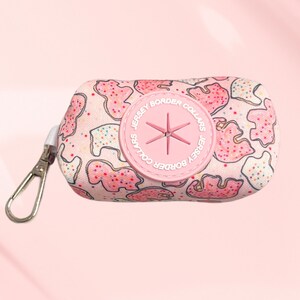 May include: Pink dog poop bag holder with a white background and a pattern of pink and white cookies. The holder has a pink circle with the text "Jersey Border Collars" and a star in the center.