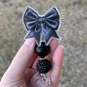 May include: Black and silver glitter bow with black rhinestone beads and a clear plastic retractable badge holder.