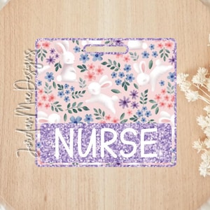 May include: A purple and pink glitter badge holder with a floral pattern and white bunnies. The text "NURSE" is on the bottom of the badge holder.