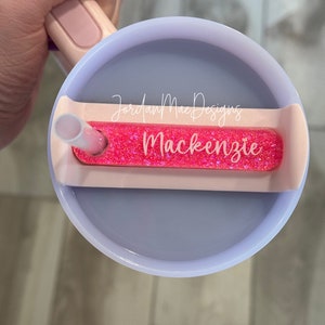 Puede incluir: Un vaso rosa y blanco con una tapa de purpurina rosa y una pajita. La tapa tiene un inserto de purpurina rosa con el texto "Jordan Mae Designs Mackenzie" en &eacute;l.